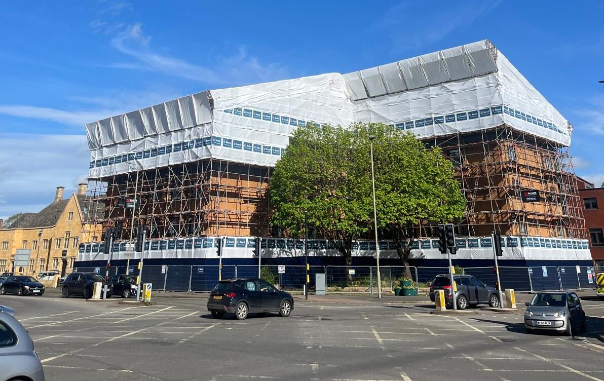 a portrait photo of the town house in banbury with temporary roof, protective sheets, a clear blue sky takes 60% of the space in the photo, highlighting the temporary roof and scaffolding
